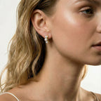 14K gold-plated curved stud earrings with three white freshwater pearls aligned vertically on cream background