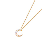 Gold crescent moon pendant with graduated white pearls on delicate chain against cream background
