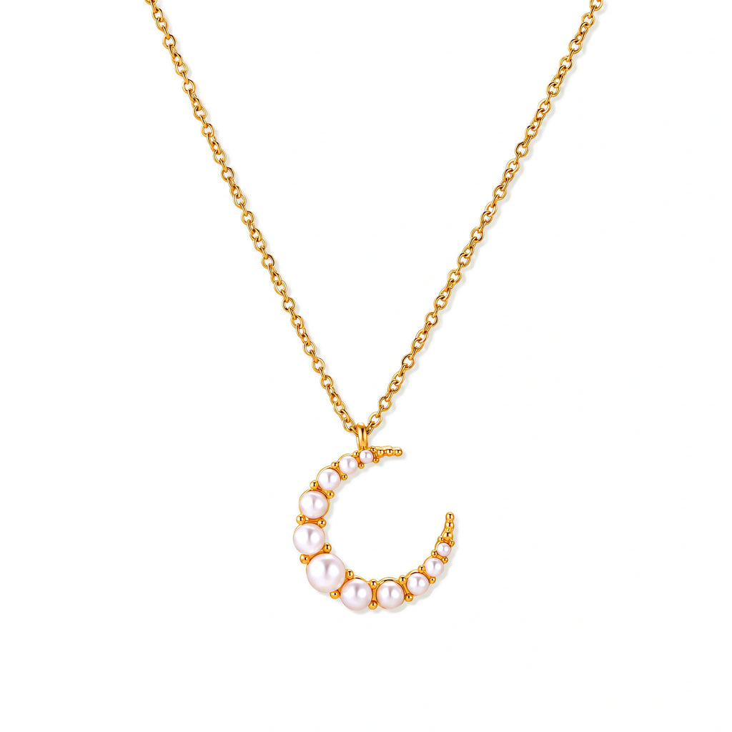 Gold crescent moon pendant with graduated white pearls on delicate chain against cream background