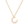 Gold crescent moon pendant with graduated white pearls on delicate chain against cream background